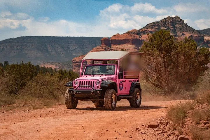 Ein rosa offener Jeep auf einer roten Schotterstraße unter den roten Felsen von Sedona