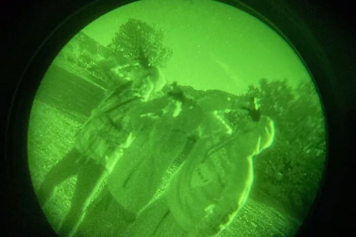 Der Blick durch eine Nachtsichtbrille: ein grün leuchtendes Bild von Bäumen und Gestalten bei Nacht